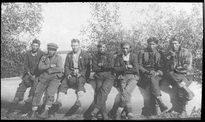 Photograph of seven men sitting on a canoe at Albany River